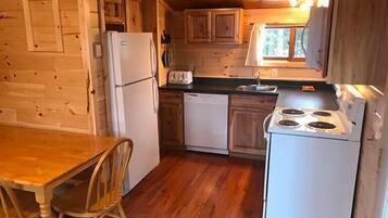 Una cocina compacta con armarios de madera, un refrigerador, un lavavajillas, una estufa y una mesa de comedor con sillas.