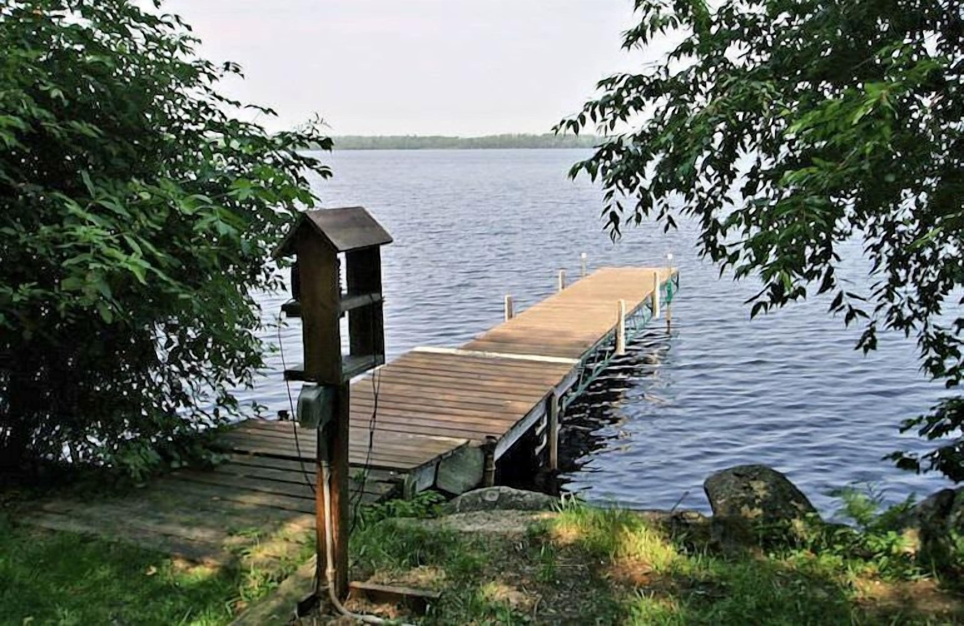 A wooden dock extending into a calm lake, surrounded by lush greenery.