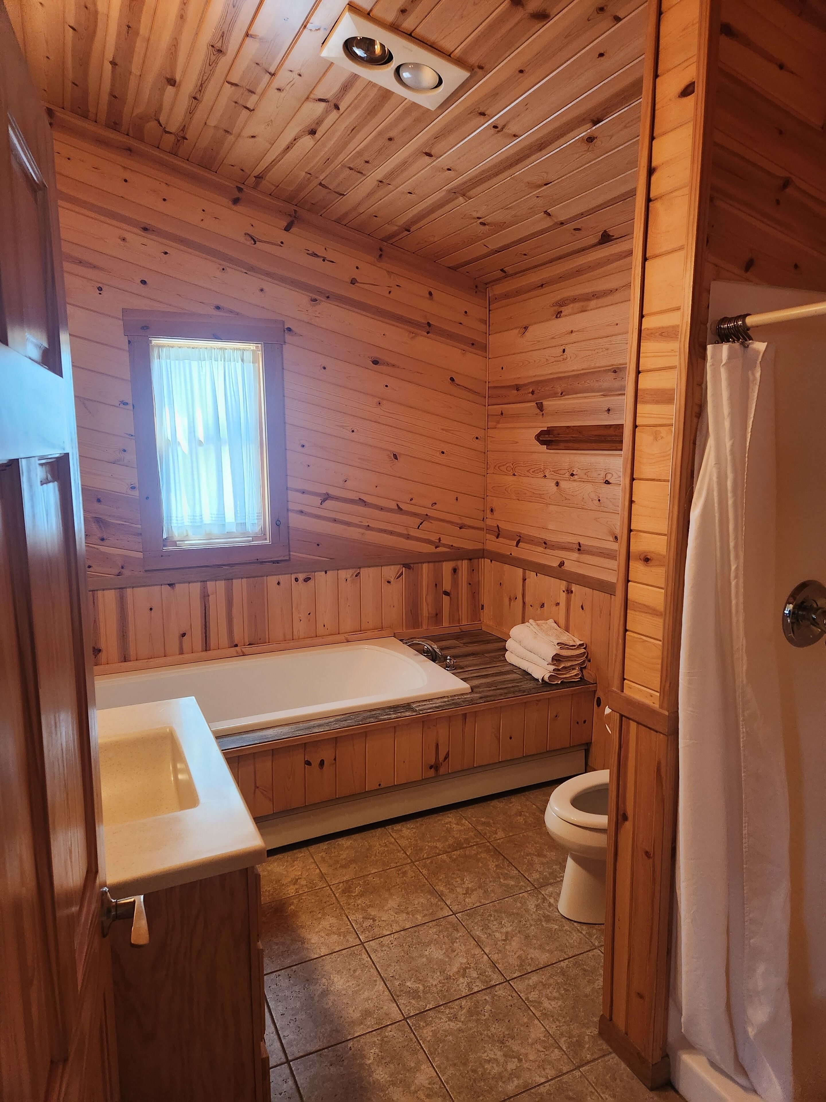 A wooden cabin bathroom with a bathtub, toilet, and sink.