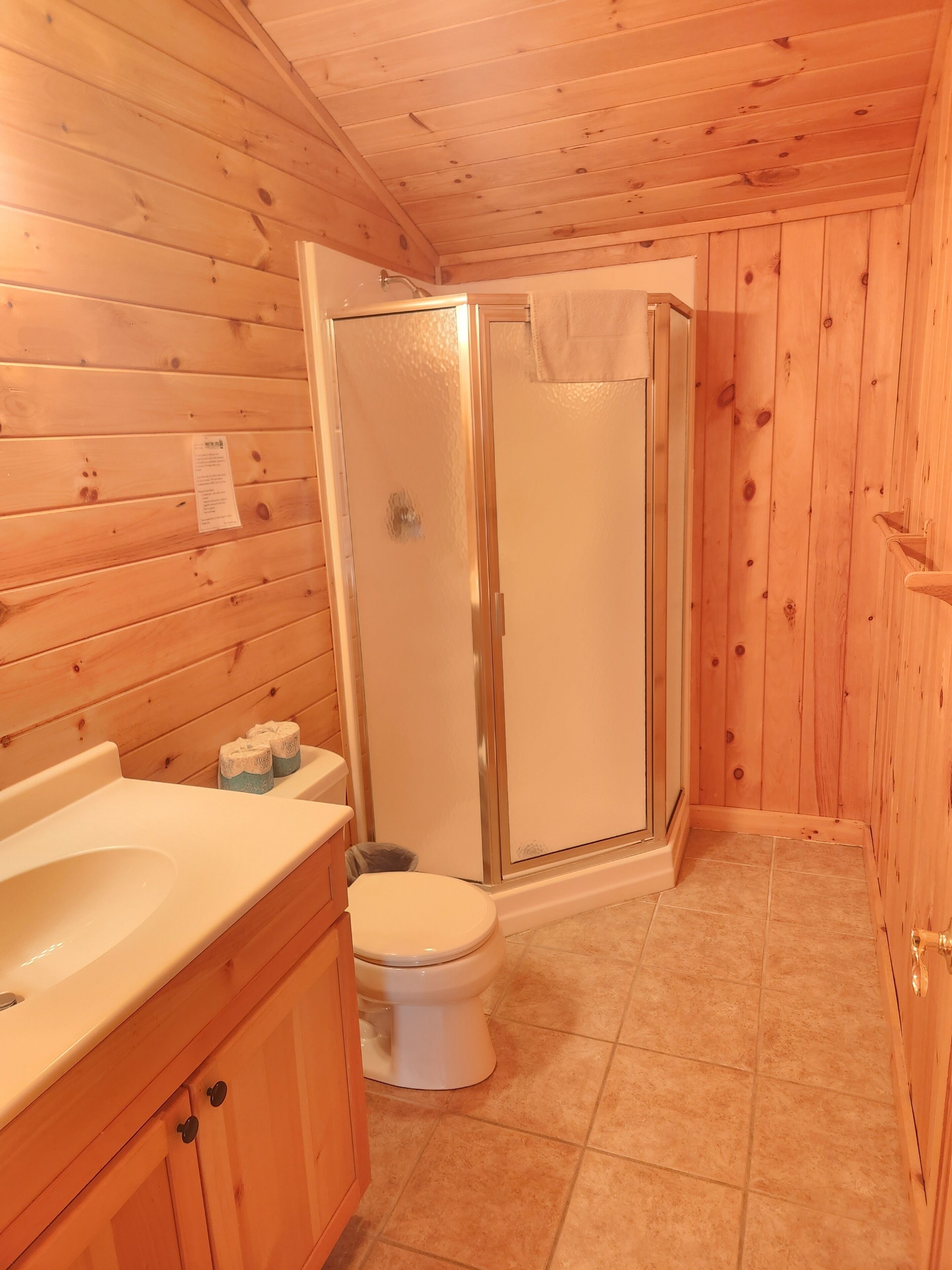 A wooden cabin bathroom with a shower, toilet, and sink.