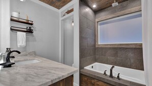 A modern bathroom with a marble sink, wooden vanity, and a stone-tiled bathtub. - Cozy Country Cabin in the Woods (Dayton)