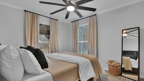 A bedroom with a bed, a ceiling fan, a large mirror, and a window with curtains. - Cozy Country Cabin in the Woods (Dayton)