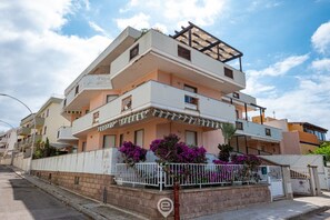 Un immeuble résidentiel à plusieurs étages, doté de balcons, d’une entrée sécurisée et d’une allée pavée.