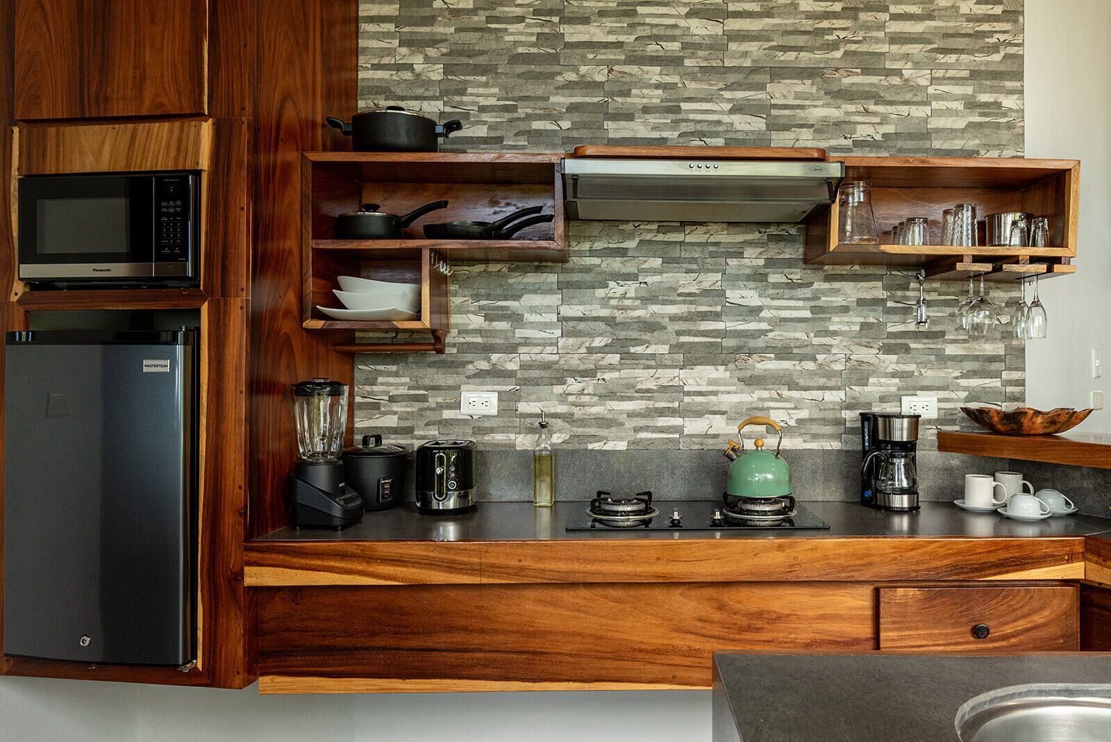 A modern kitchen with wooden cabinetry, a built-in microwave, a gas stove, a blender, a kettle, and various kitchen utensils.