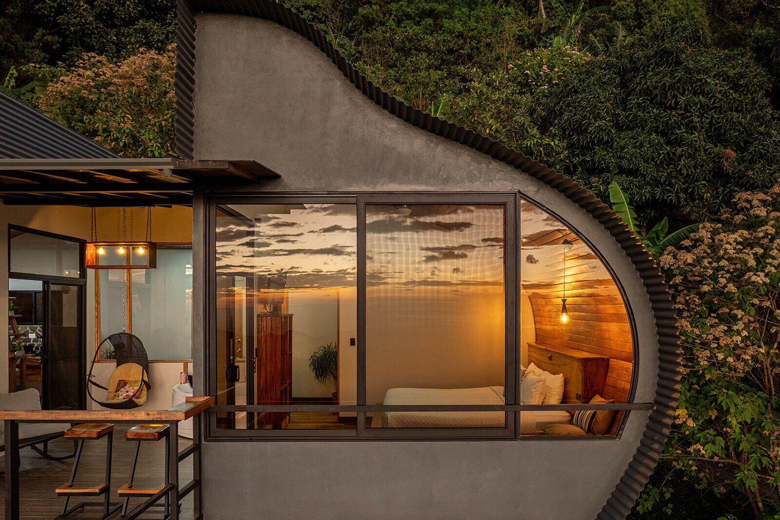 A modern, curved exterior of a building with a glass window revealing a bedroom interior.