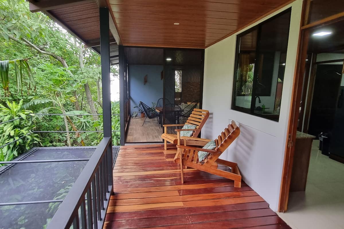 Terraza de madera con sillas y una mesa, con vistas a exuberante follaje.