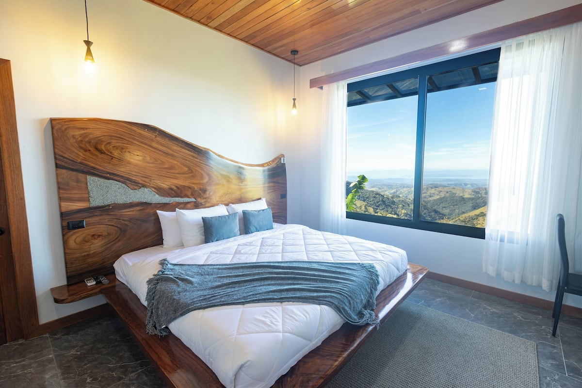 Un dormitorio con una cama grande, cabecero de madera y vistas a un paisaje a través de una ventana.