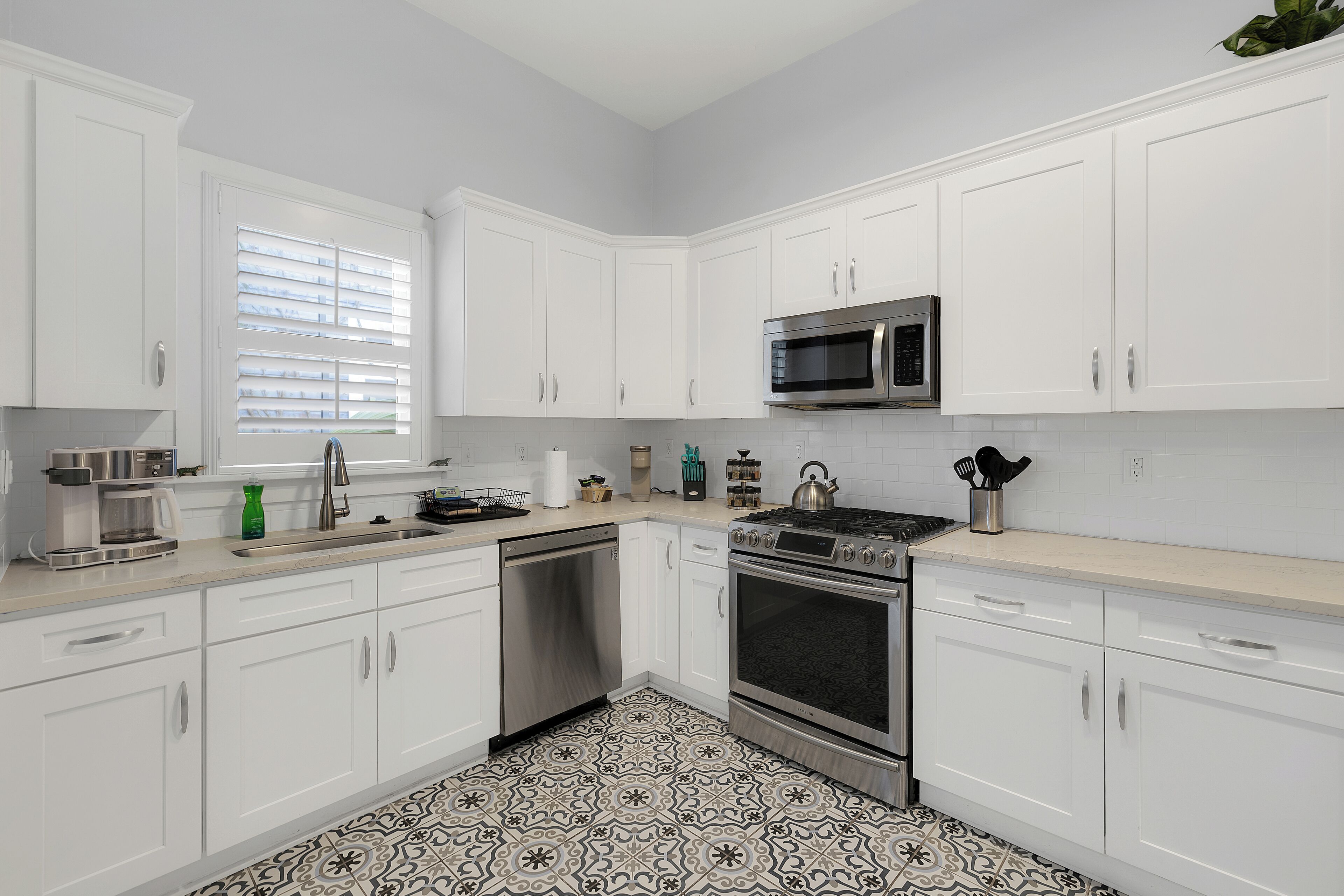 Una cocina moderna con armarios blancos, electrodomésticos de acero inoxidable y baldosas de suelo con diseños.