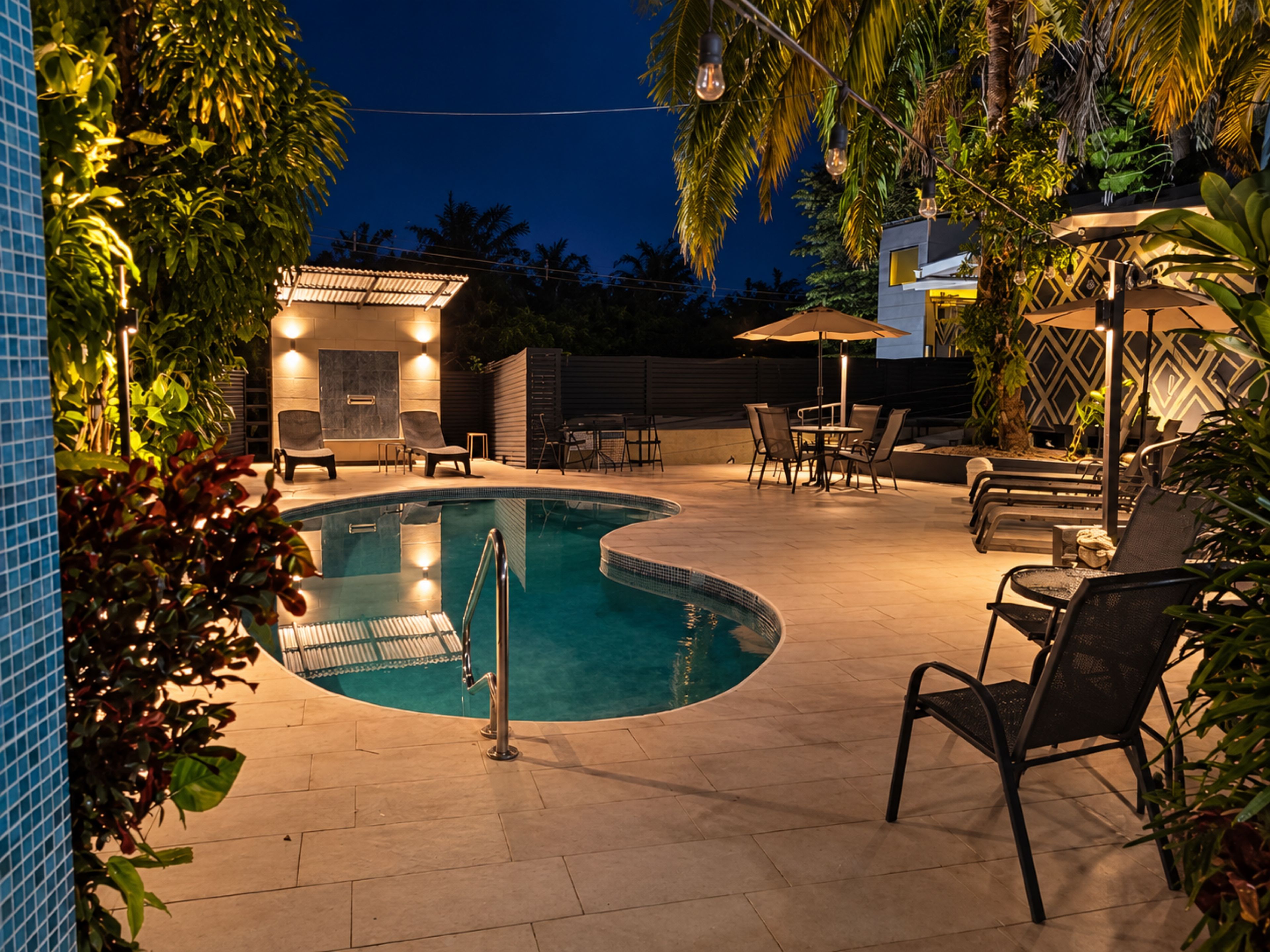 A swimming pool with a curved edge, surrounded by lounge chairs and a table with umbrellas.