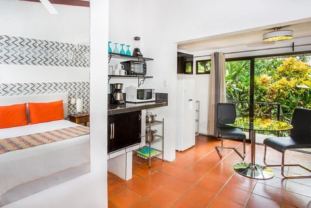 Een moderne hotelkamer met een bed, kitchenette en een balkon met uitzicht op groen.