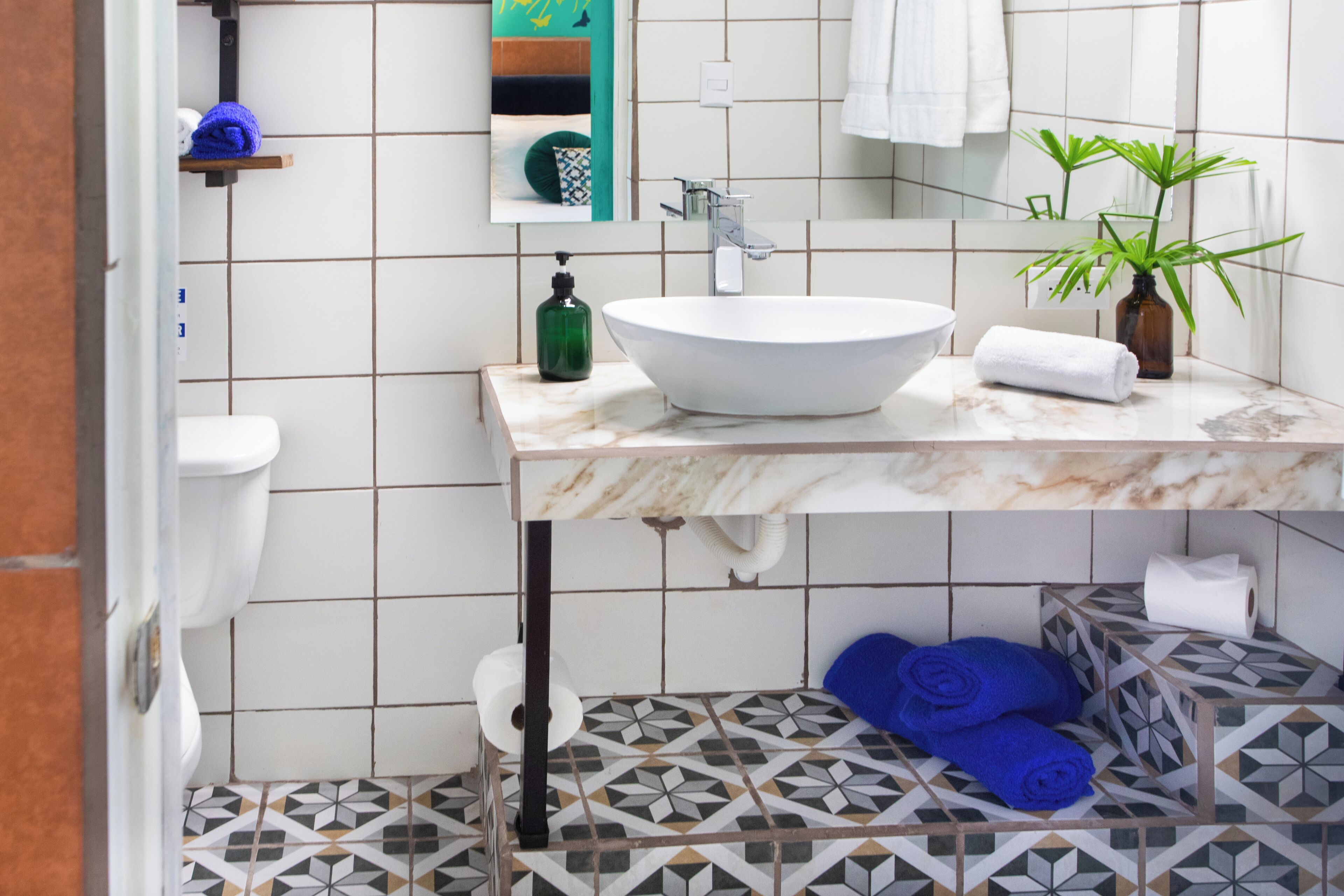 A bathroom with a white sink, a mirror, a green bottle, and a potted plant.