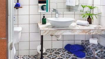 A bathroom with a white sink, a mirror, a green bottle, and a potted plant.