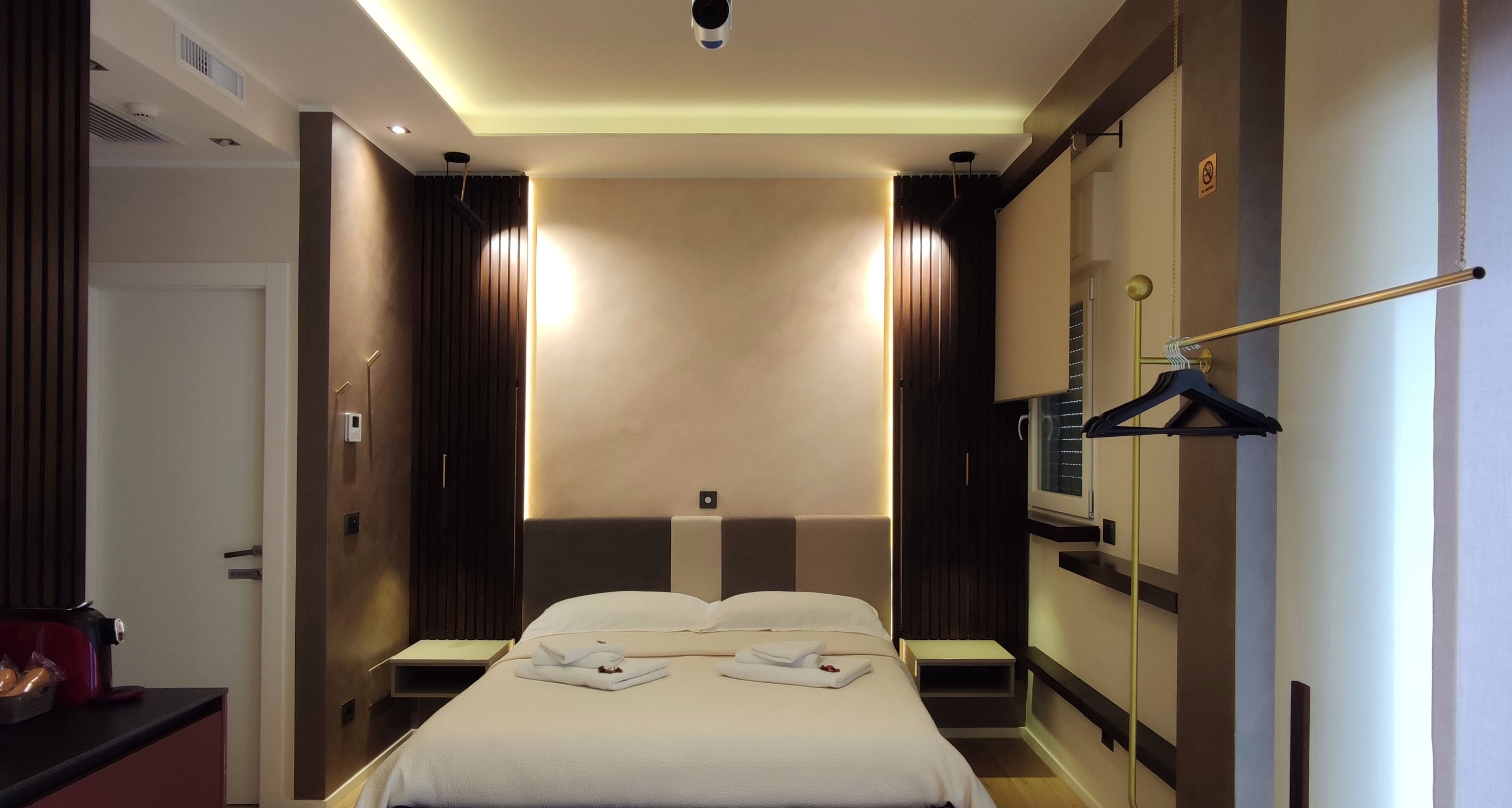 Una habitación de hotel moderna con una cama bien hecha, mesitas de noche, un armario y un perchero.