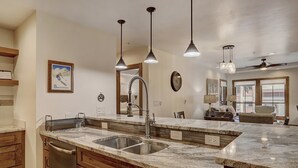 A kitchen with a large island, stainless steel sink, wooden cabinets, pendant lights, and a clock on the wall. - Premier Ski Condo w/ Slopeside Access (Breckenridge)