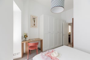 A bedroom with a bed, a desk, a chair, a wardrobe, and a hanging light fixture.