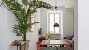 A dining area with a wooden table, chairs, a potted plant, a vase with flowers, and a television on a stand. - iFlat | Soft & Relaxing apt in Trastevere (Roma)