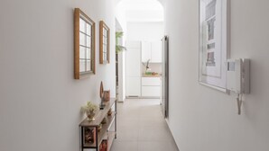 A hallway with framed pictures, a small table with a vase, and a kitchen in the background. - iFlat | Soft & Relaxing apt in Trastevere (Roma)