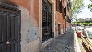 A narrow cobblestone street with parked cars and a building with a large metal gate and a small window. - iFlat | Soft & Relaxing apt in Trastevere (Roma)