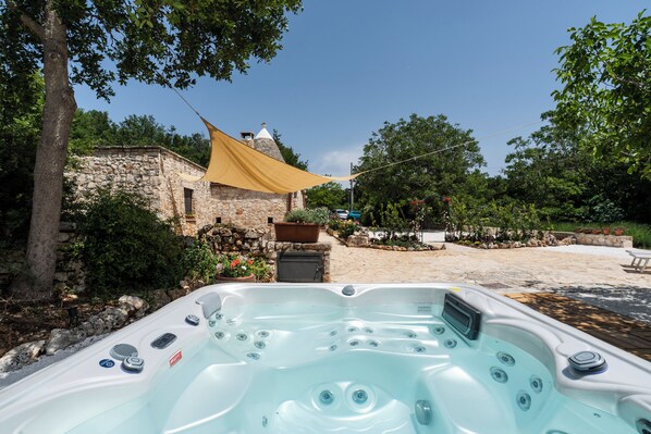 Un bain à remous dans un jardin, avec un bâtiment en pierre et un auvent jaune.