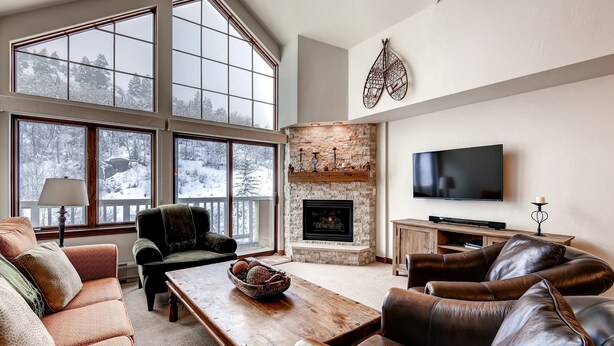 A spacious living room with large windows, a fireplace, leather sofas, and a flat-screen TV.
