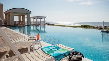 Un espace aménagé au bord de la piscine, avec des chaises longues, une petite table et une vue sur l’océan.