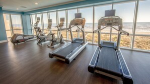 Une salle de sport équipée de tapis de course, de vélos elliptiques et d’un rameur, avec de grandes fenêtres donnant sur la plage.