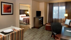 Ein Hotelzimmer mit Bett, Schreibtisch mit Laptop, Fernseher und Essbereich mit Tisch für zwei Personen.