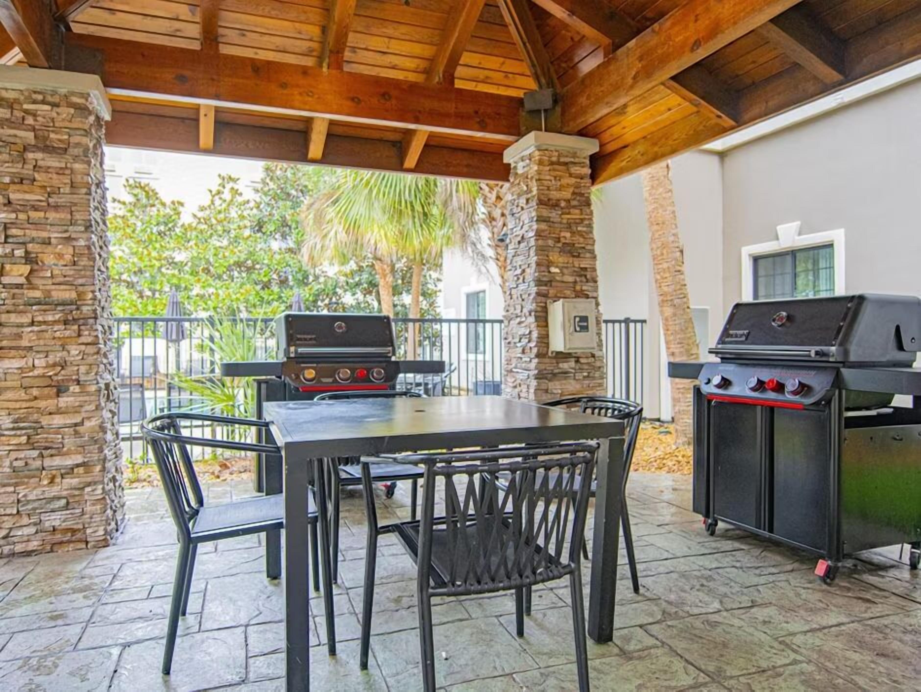 Un patio exterior con pilares de piedra, una mesa y dos parrillas de barbacoa.
