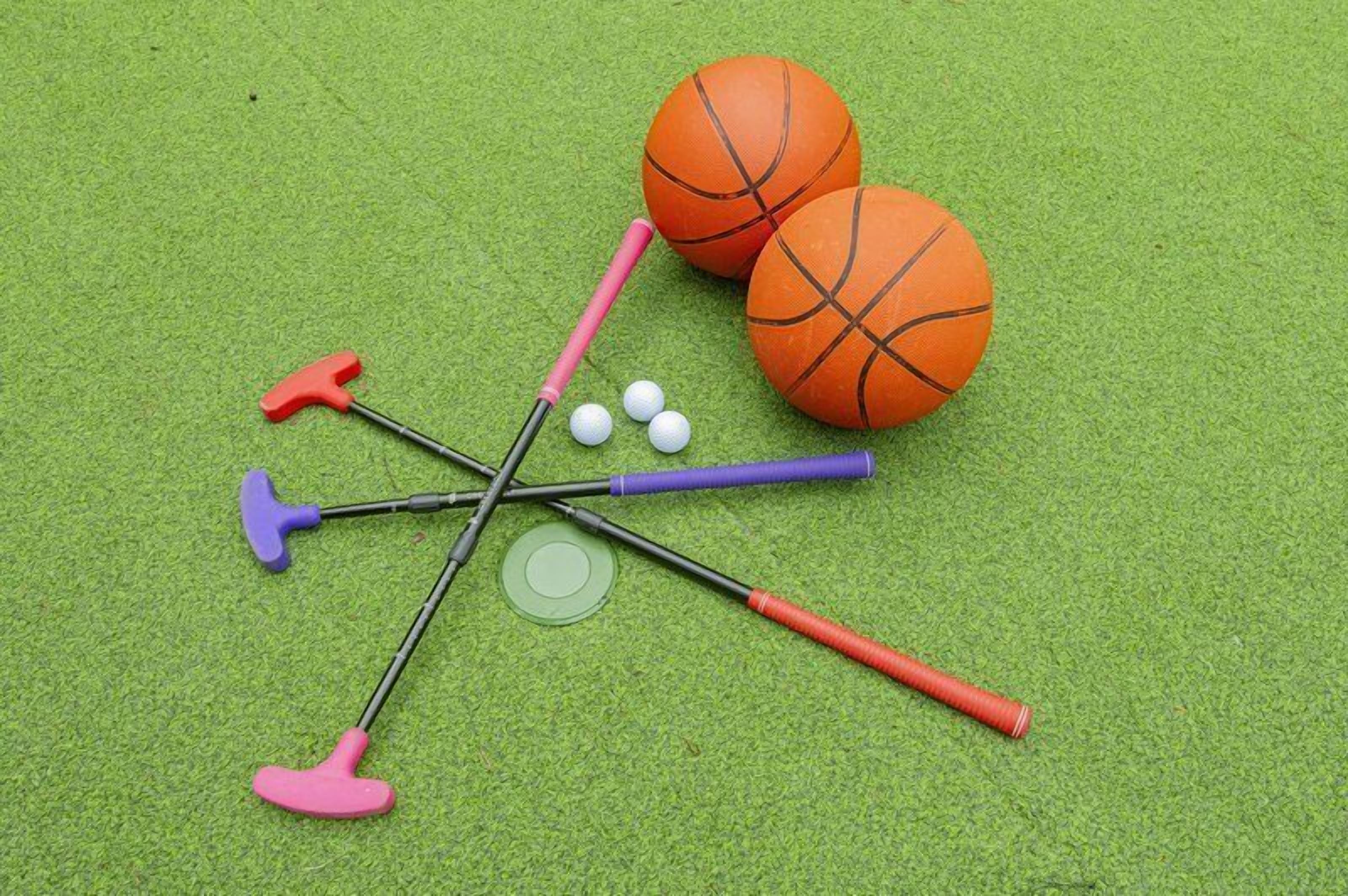 A green surface with a basketball, three golf clubs, and three golf balls.
