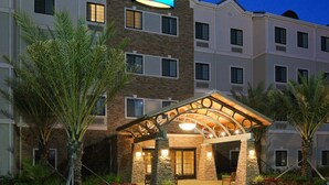 A Staybridge hotel with a stone facade, multiple windows, and a covered entrance area with seating. - Queen Studio Suite | Full Kitchen Included (Lafayette)