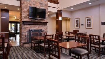 A restaurant with wooden tables and chairs, a stone fireplace, and a flat-screen TV mounted on the wall.