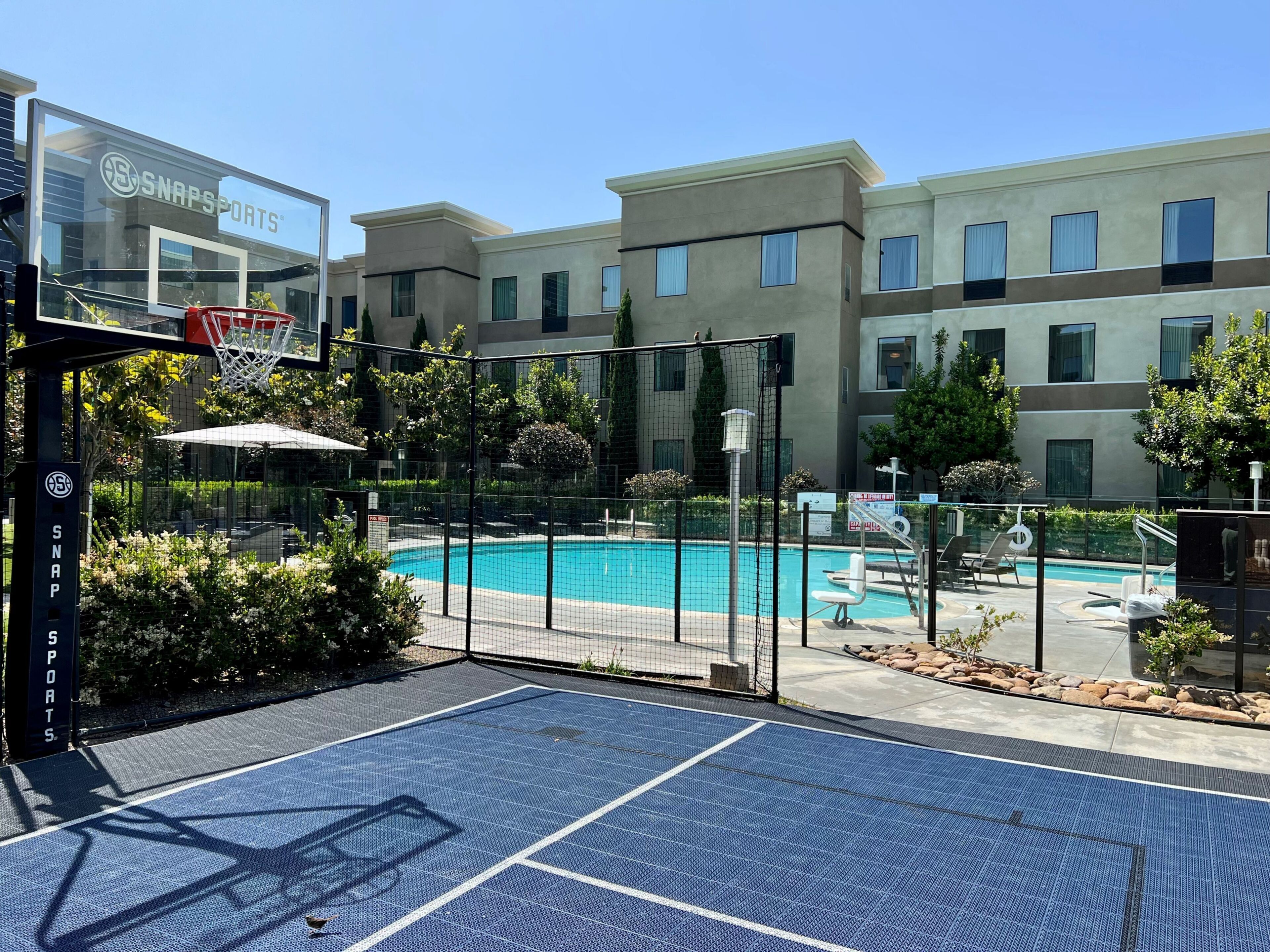 A pool area with a basketball court, a fence, and a building with a sign.