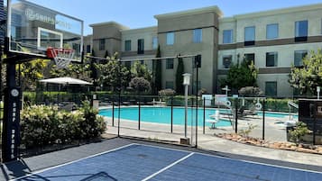 A pool area with a basketball court, a fence, and a building with a sign.