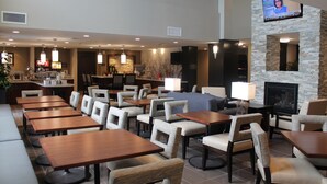 Un vaste espace intérieur aménagé avec différents coins salon, comprenant des tables et des chaises, un téléviseur fixé au mur et une cheminée en pierre.