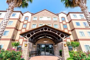 A multi-story hotel with a central entrance, stone facade, and symmetrical windows. - Free Breakfast Buffet + Outdoor Pool | Comfy Suite (Houston)