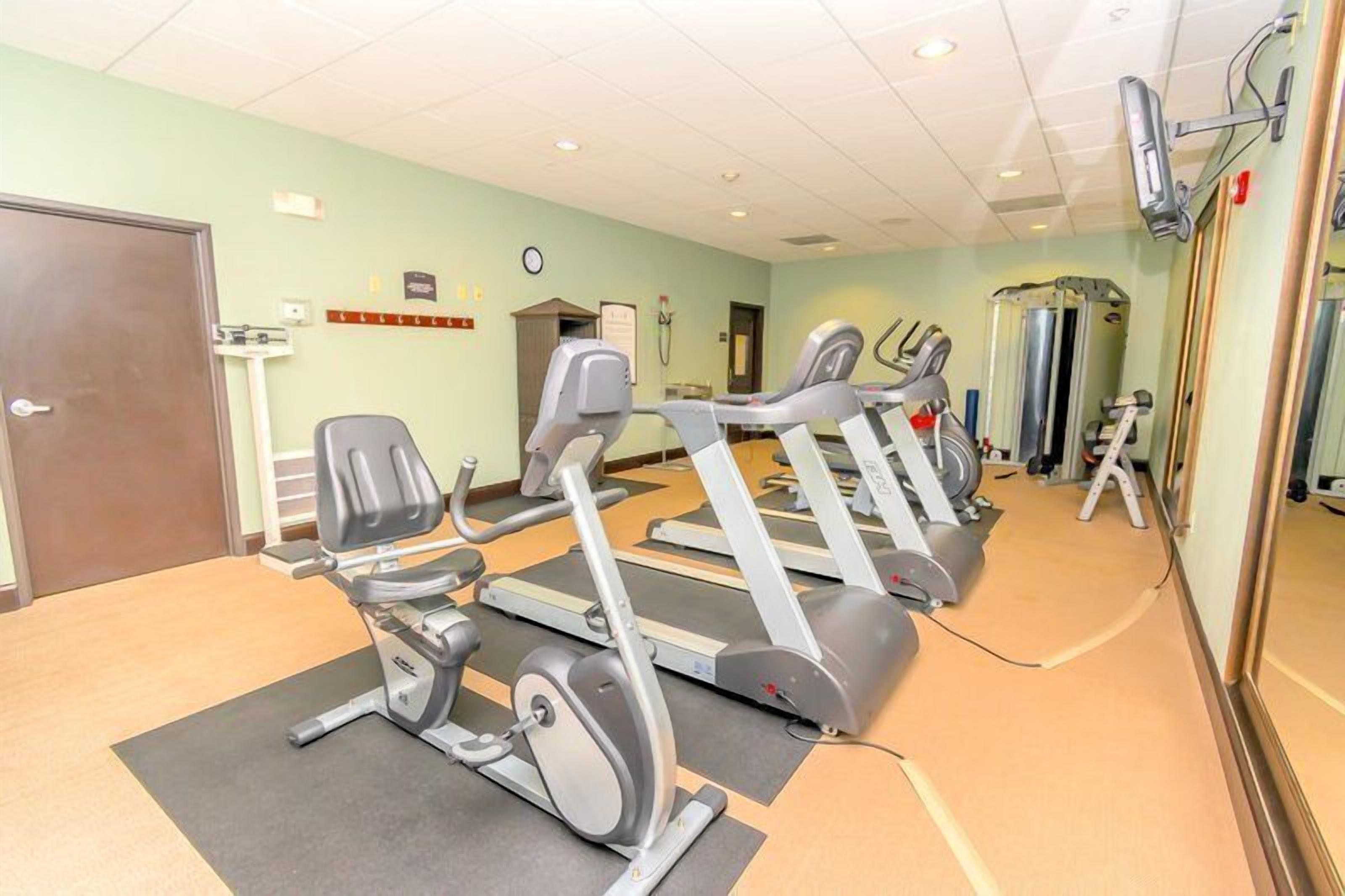 A gym with stationary bikes, a treadmill, and a mirror wall.