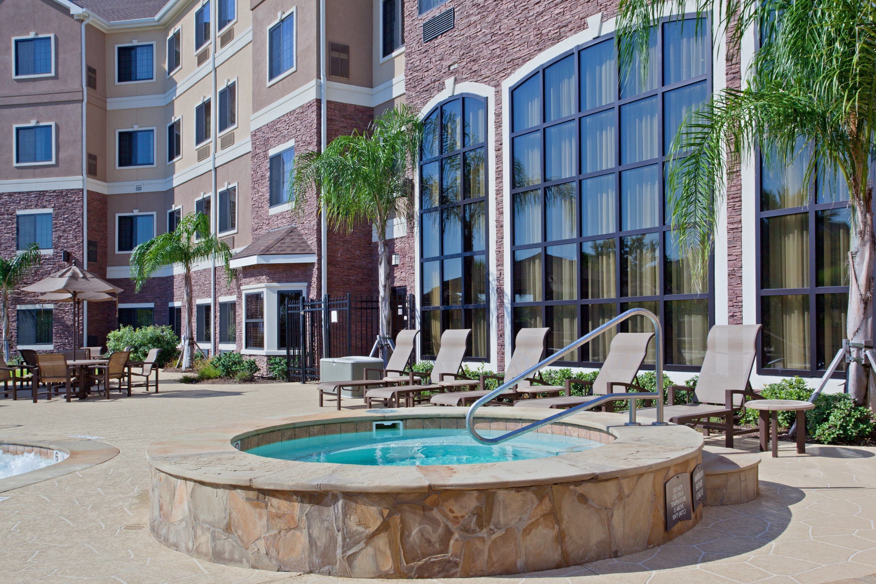 Un espace piscine d’hôtel comprenant des chaises longues, un jacuzzi et une piscine dont le fond est recouvert de pierres.