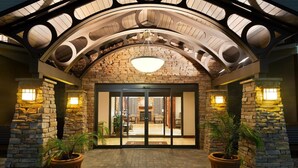 Una entrada de hotel con fachada de piedra, puerta de vidrio y suelo de ladrillo.