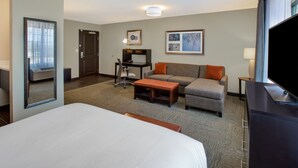 Une chambre d’hôtel comprenant un lit, un bureau avec une chaise, un canapé avec des coussins, une télévision et un tableau encadré au mur.