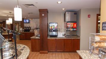 Een ontbijtruimte in een hotel met een koffieapparaat, een koelkast en een buffetopstelling.