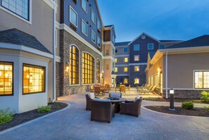 A courtyard with outdoor seating, stone walls, and multiple buildings with large windows.