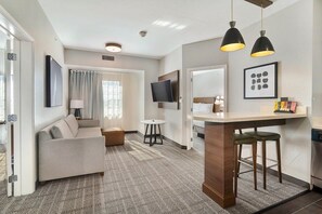 Habitació d'hotel moderna amb sofà, una taula petita, televisió i una cuineta.