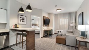 A modern hotel room with a kitchenette, a dining area, a living area with a sofa and armchair, and a TV mounted on the wall. - 2 Bedroom | Free Breakfast. Indoor Pool (Longview)