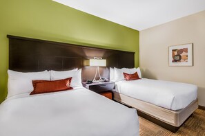 Two single beds with white linens and brown pillows, a dark headboard, and a bedside table with a lamp.