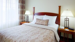 Habitación de hotel con una cama grande, dos mesitas de noche con lámparas, un teléfono y un control remoto sobre una de ellas.