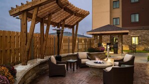 An outdoor patio with a wooden pergola, seating area, and a fire pit.