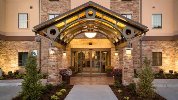 A hotel entrance with a stone facade, a covered entrance, and potted plants.