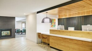 Un área de recepción moderna con mostrador de madera, chimenea y comedor con sillas.