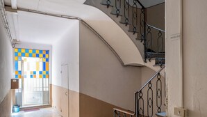 A hallway with a staircase leading to an upper floor. The hallway has a tiled floor and a door with a colorful window. - Appartamento vicino all'Orto Botanico by Wonderful Italy (Bologna)