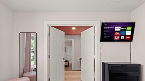 A hotel room with a large mirror, a TV mounted on the wall displaying streaming services, a bedside table, and a bed. - Pool, Pickleball, Resort Backyard, 16min to Downtown - Modern Cowgirl (Austin)